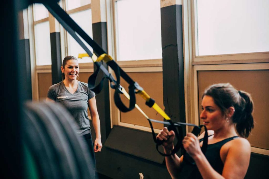 Vrouw traint met TRX onder toezicht van personal trainer voor small group training